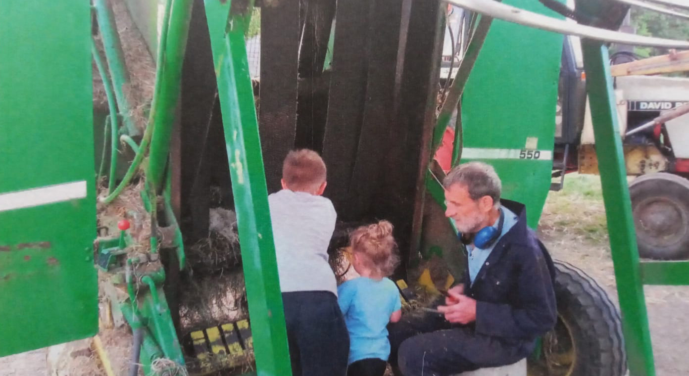 Family photo of John Philip Charlesworth with his grandchildren near farm equipment.