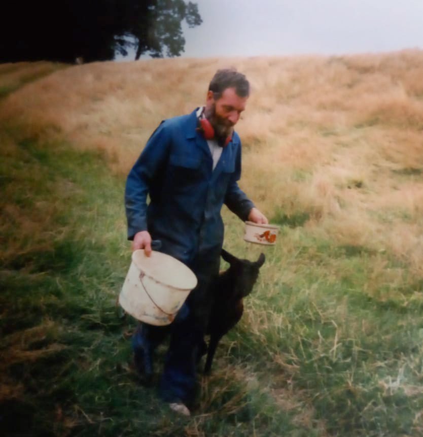 Photo of John Philip Charlesworth, a farmer, walking in a field with a bucket and a small animal.